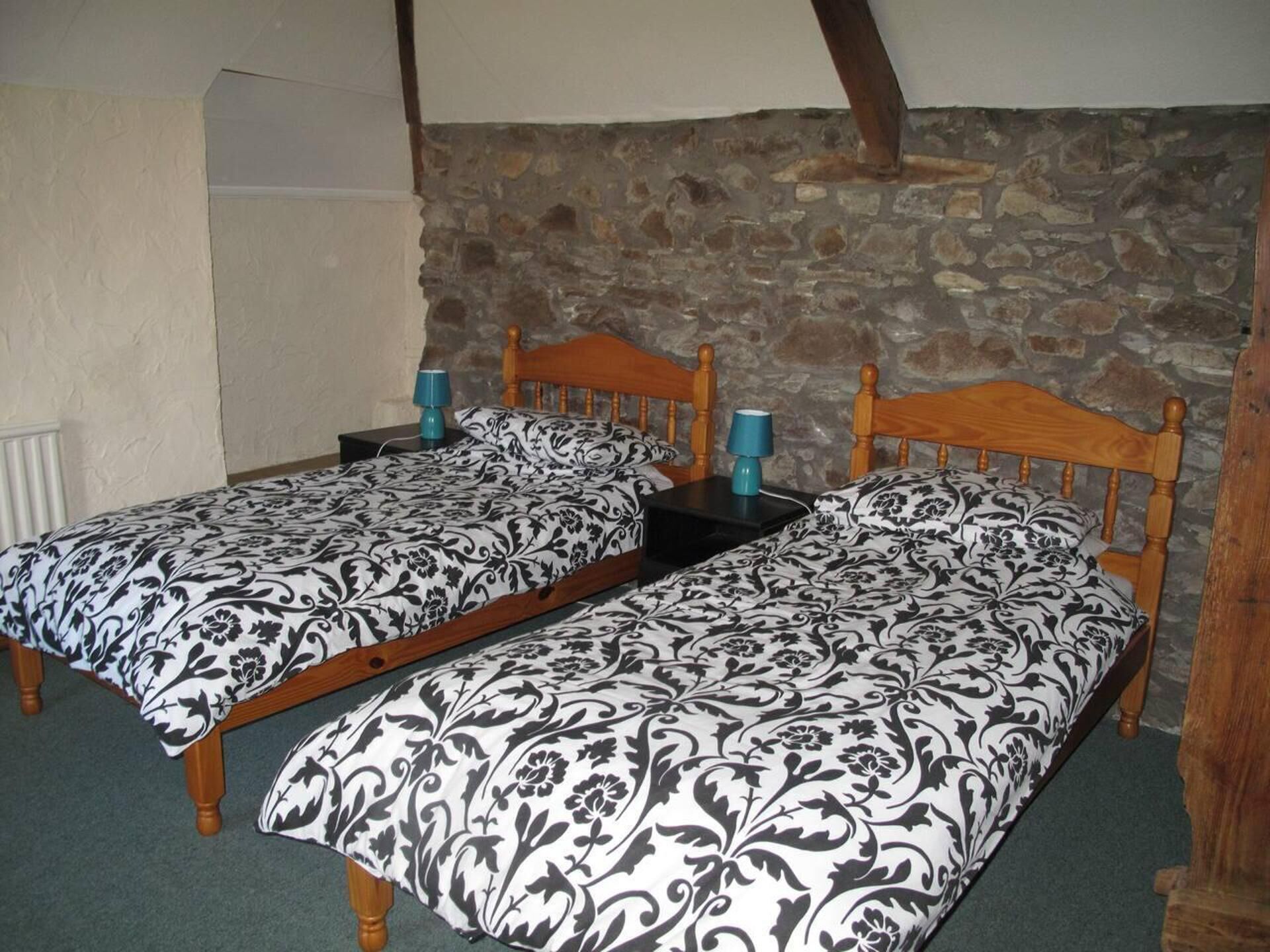 Een kamer met twee houten bedden, elk met een bijpassend hoofdbord, een stenen muur en een witte radiator.