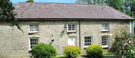 A stone building with a sloped roof, three windows, and a small door.