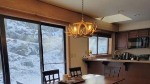 A modern kitchen with a dining area, large windows, and a view of a snowy landscape. - Fox'em Falls (Roseland)