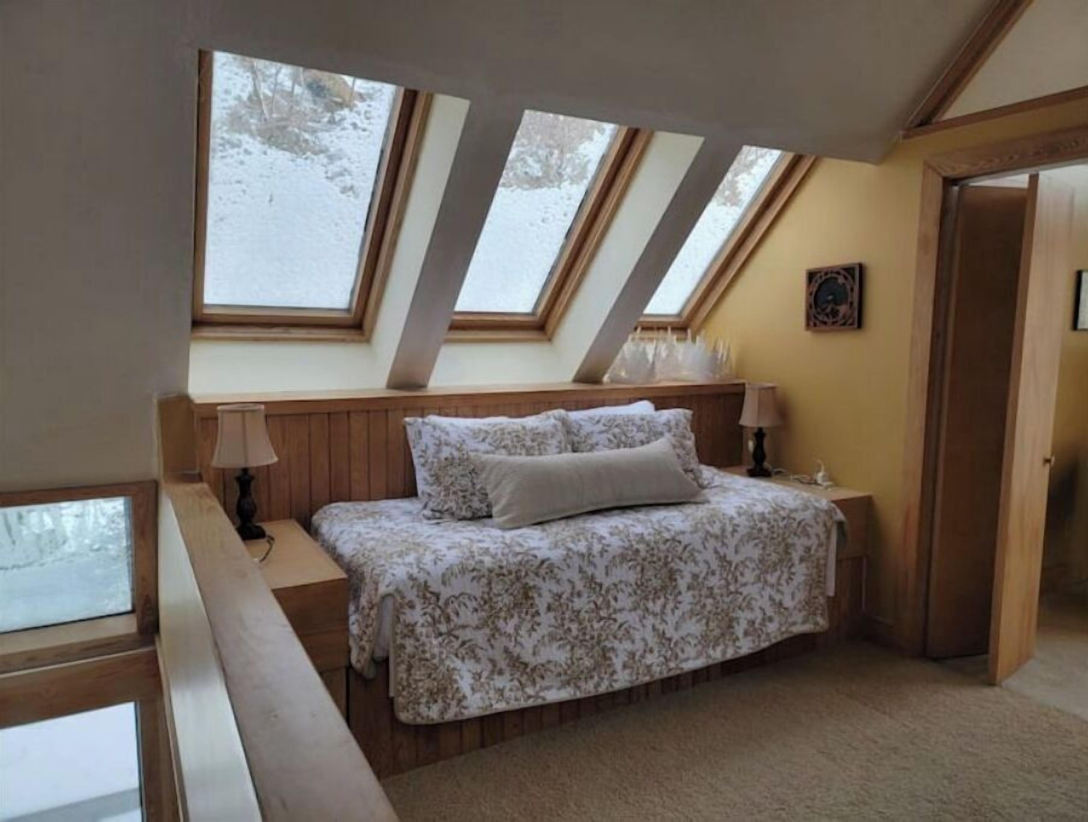 Een slaapkamer met een schuine kap, dakramen, een bed met bloemenbeddengoed, een nachtkastje en een lamp.