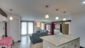 Un amplio espacio de sala con un sofá gris, una mesa de comedor con mantel rojo y blanco, y una isla de cocina con encimera de granito.
