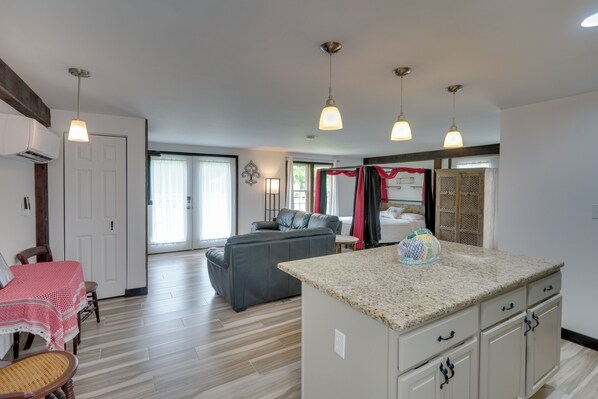 Un amplio espacio de sala con un sofá gris, una mesa de comedor con mantel rojo y blanco, y una isla de cocina con encimera de granito.