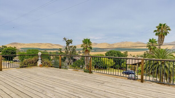 A wooden deck with a metal railing, overlooking a landscape with palm trees and distant mountains. - Porterville Getaway w/ Patio + Valley Views! (Porterville)