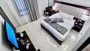 A modern hotel room with a large bed, a desk with a computer, a TV, and a nightstand with a lamp. - Petra Icon Hotel (Wadi Musa)
