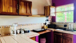 Une cuisine avec des meubles en bois, un îlot central aux lignes courbes et un mur d’accent de couleur violette.