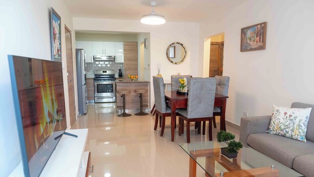 A modern living room with a glass coffee table, grey sofa, and a dining area with a wooden table and grey chairs.