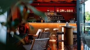 A bar area with wicker chairs, a tiled floor, and a red wall with shelves of bottles. - Rupa Experience Alacati (Cesme)