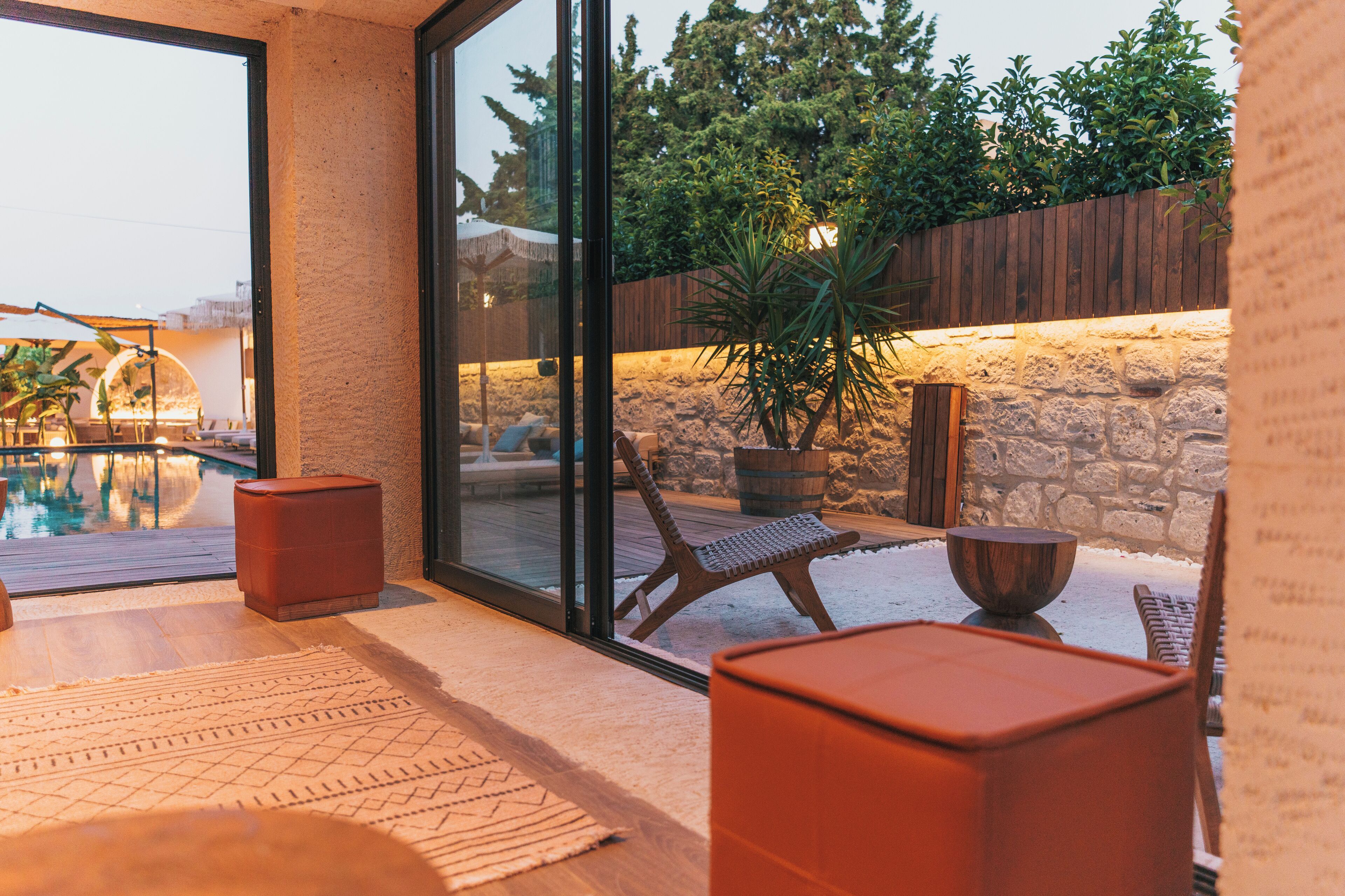 A modern outdoor patio with a pool, stone wall, and wooden deck furniture.