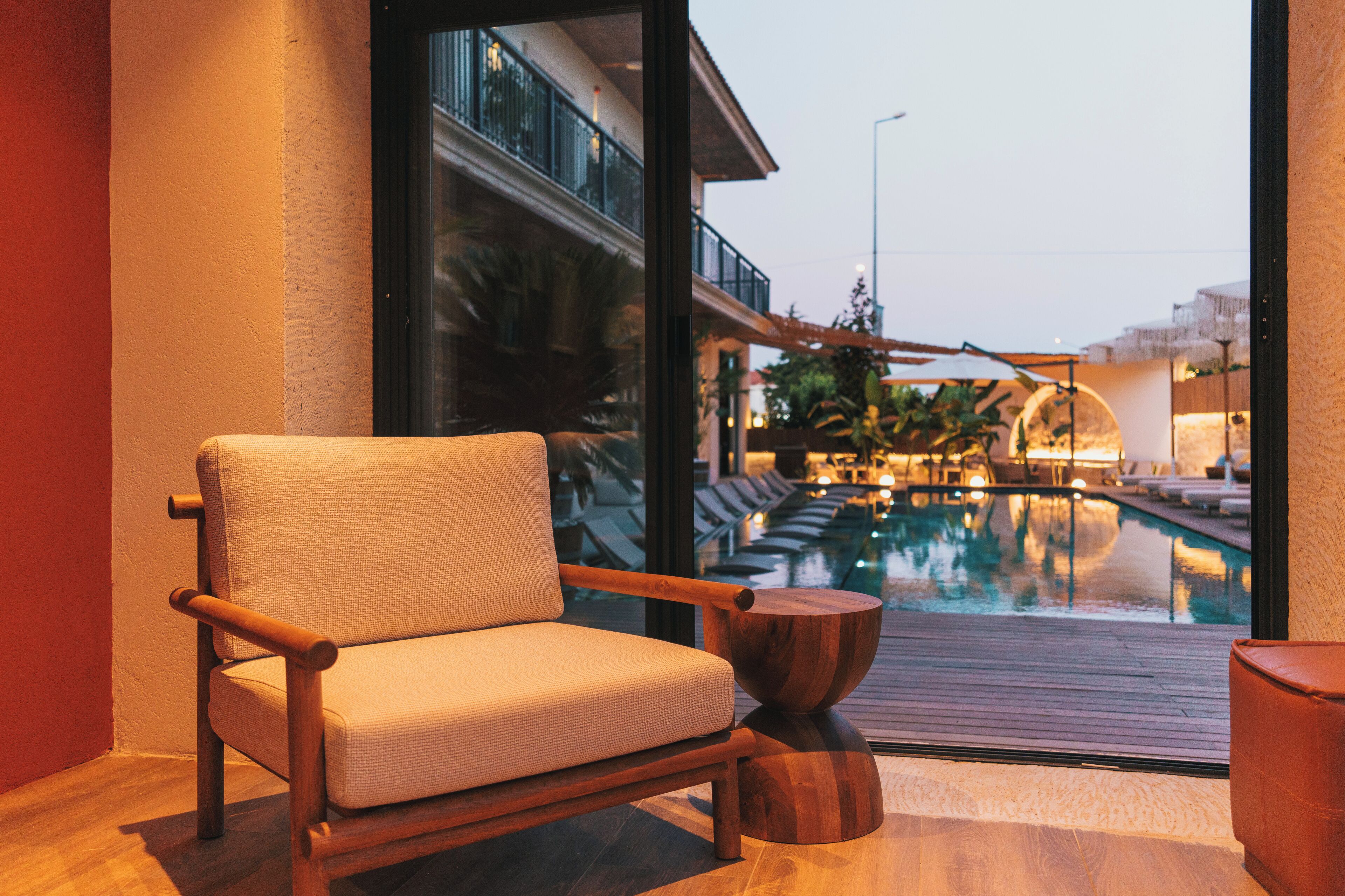 A modern lounge area with a cushioned chair, a wooden side table, and a view of an outdoor swimming pool.