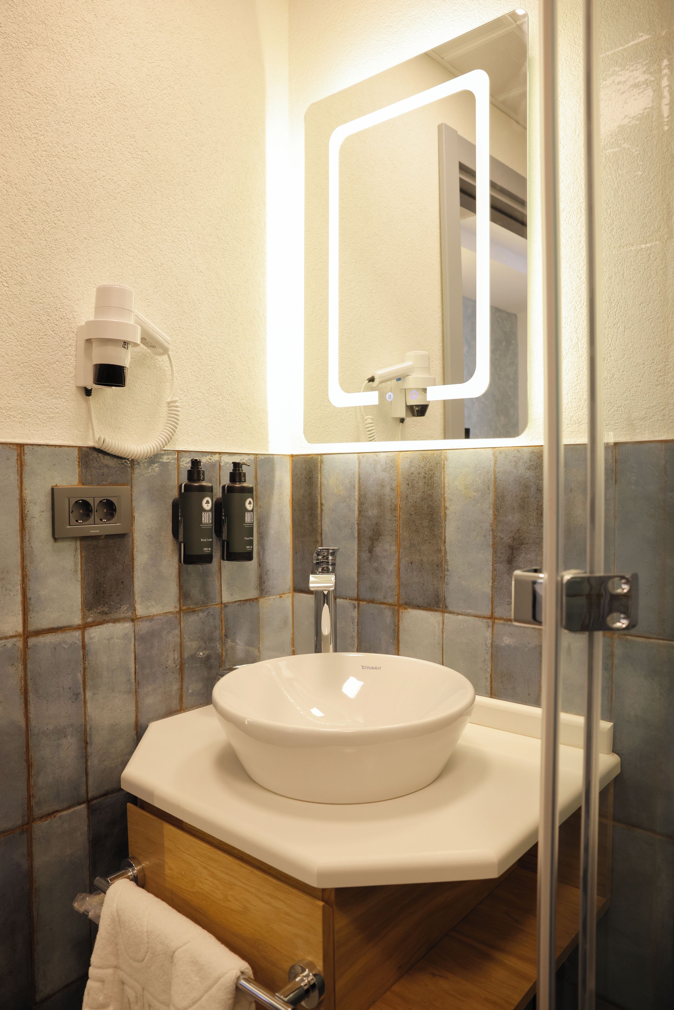 A bathroom with a white sink, a mirror with a light, a towel rack, and a hairdryer.