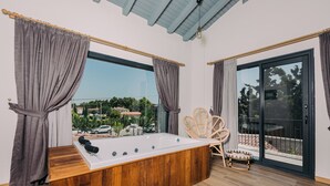 A modern bathroom with a wooden bathtub, large windows, and a wicker chair. - Rupa Experience Alacati (Cesme)