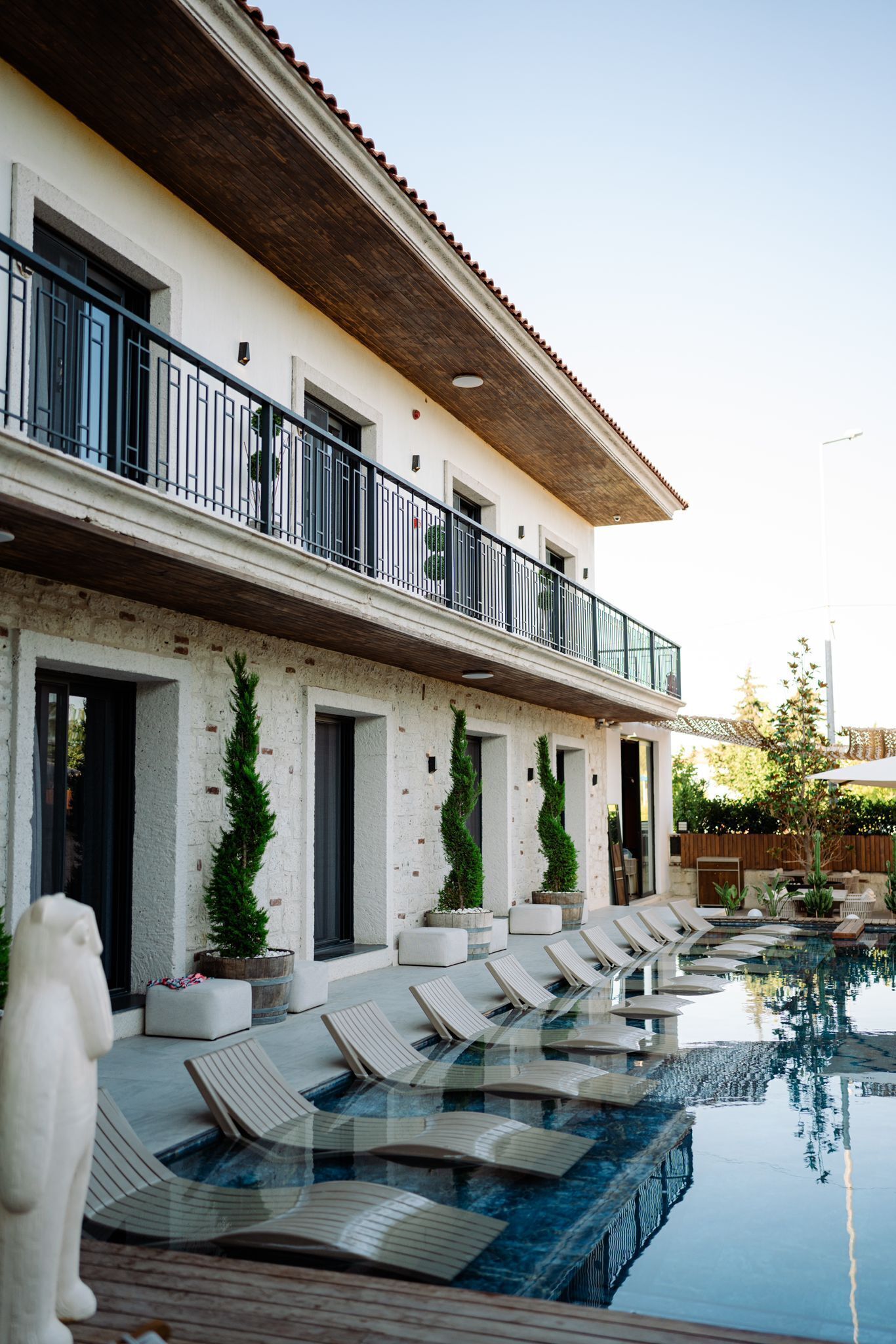 Un espace aménagé au bord de la piscine, avec des chaises longues et un bâtiment doté d’un balcon.