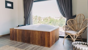 A modern bathroom with a wooden bathtub, wicker chairs, and a view of greenery outside. - Rupa Experience Alacati (Cesme)
