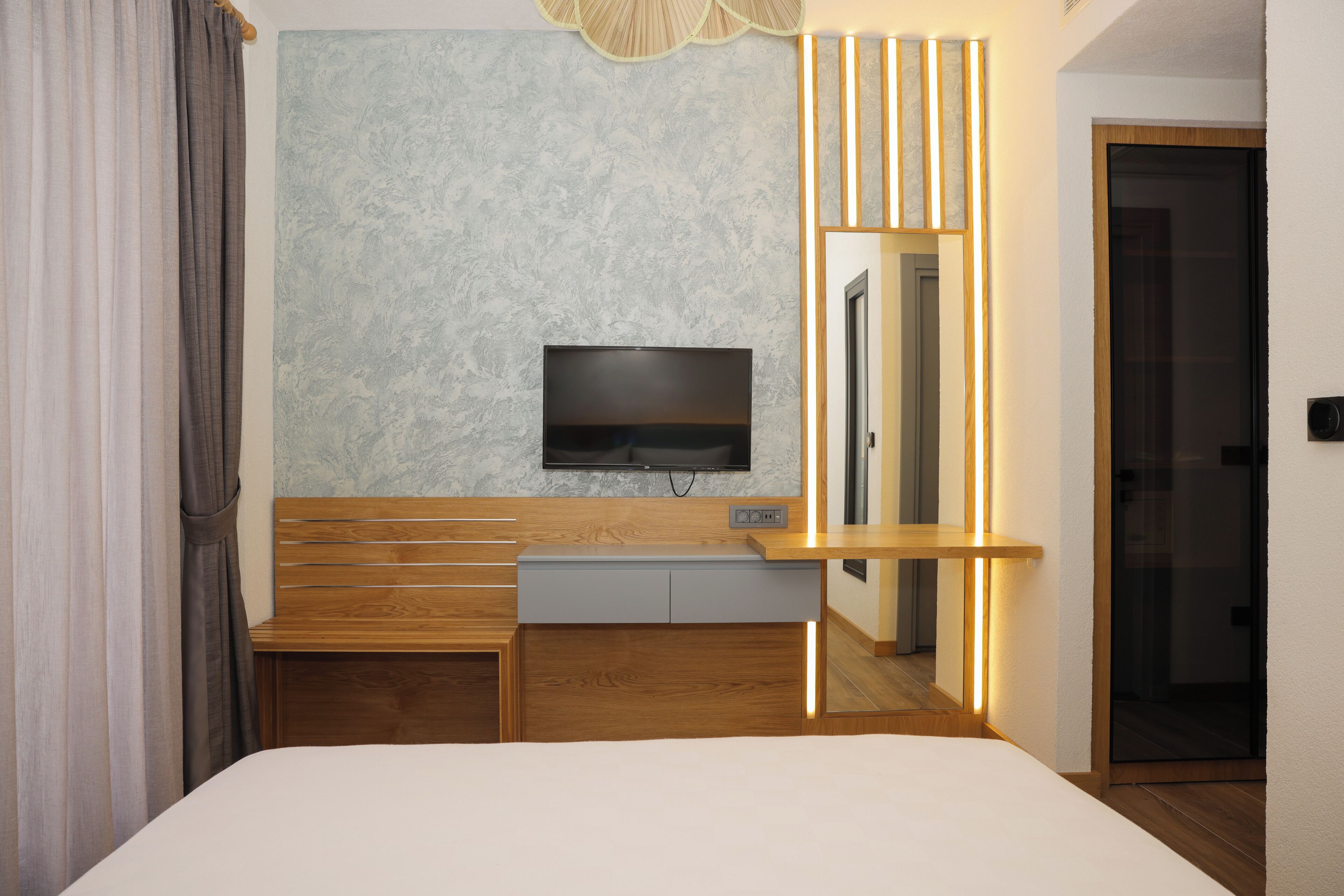 A modern hotel room with a large bed, wooden bedside tables, a built-in TV, and a mirror.
