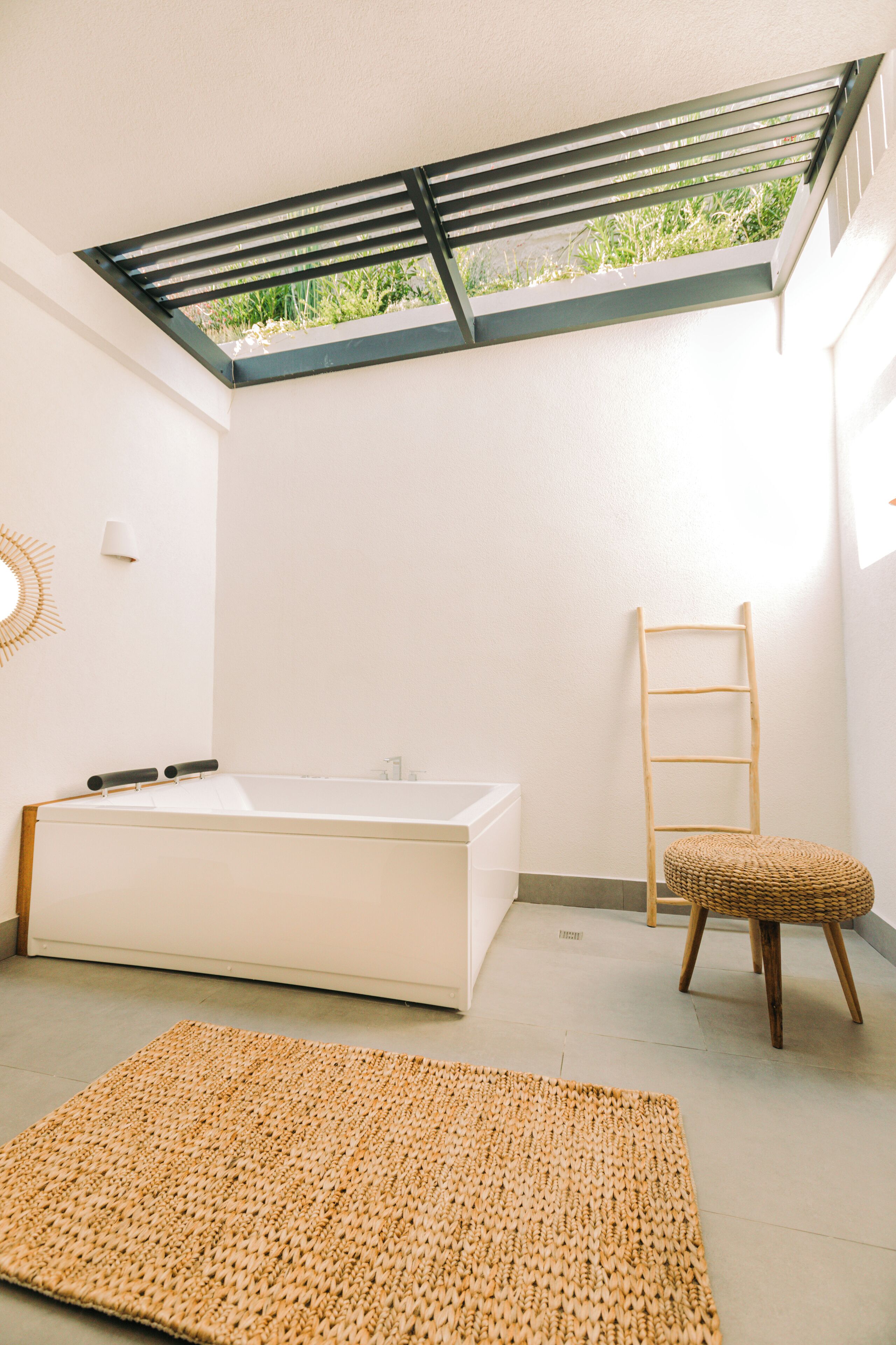 Une salle de bain moderne avec une lucarne, une baignoire, une échelle en bois et un tapis tissé.