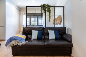 Un sofá de cuero marrón oscuro con tres cojines, una planta colgante y un adorno de pared en un salón moderno.
