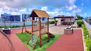 Un patio de juegos en la azotea con una estructura de madera, un tobogán y una pequeña zona de barbacoa.