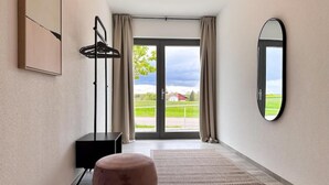 Ein modernes Hotelzimmer mit einer großen Glasschiebetür, die zu einem Garten führt, einer schwarzen Stehlampe, einem runden Hocker und einem Spiegel an der Wand.