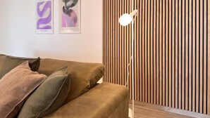 Ein modernes Wohnzimmer mit einem braunen Sofa, zwei gerahmten abstrakten Kunstwerken und einer hohen Stehlampe.