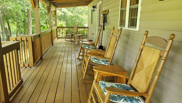 Een houten veranda met meerdere schommelstoelen en een tafel.