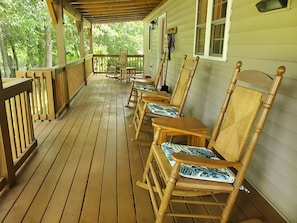 A wooden porch with several rocking chairs and a table.