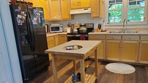 Een keuken met houten kastjes, een koelkast, een magnetron, een fornuis en een spoelbak.