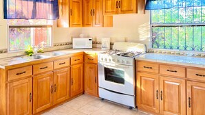A kitchen with wooden cabinets, a stove, a microwave, and a sink. - Pearl Cove Casita @ Dixon Cove (Dixon Cove)