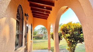 A covered outdoor area with arches and a wooden ceiling, leading to a garden with a lawn and plants. - Pearl Cove Casita @ Dixon Cove (Dixon Cove)