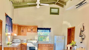 A kitchen with wooden cabinets, a stove, a refrigerator, and a window with a view of greenery. - Pearl Cove Casita @ Dixon Cove (Dixon Cove)