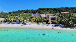 Un hotel frente a la playa con varias edificaciones, palmeras y una playa de arena.