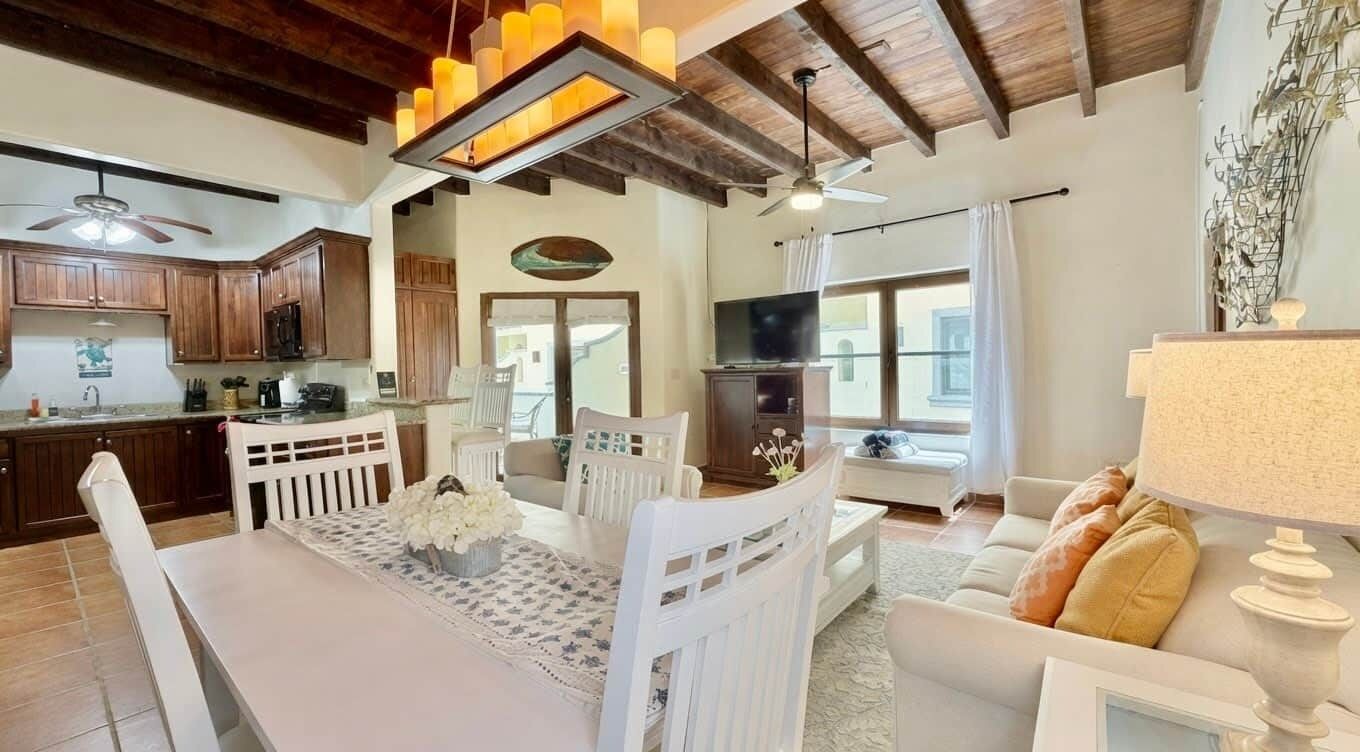 A spacious living area with a dining table, white furniture, a television, and a ceiling fan.