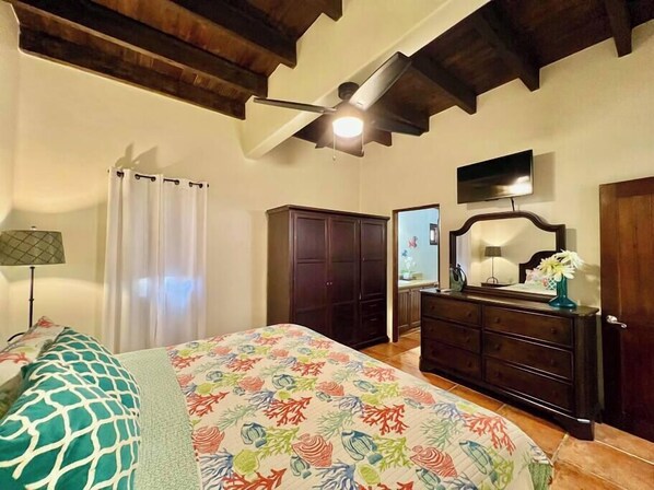 Un dormitorio con cama, cómoda, espejo, ventilador de techo y televisor.