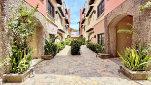 A narrow stone-paved courtyard with multiple buildings on either side, featuring balconies and arched doorways. - Mission Gate 5B @ West Bay (West Bay)