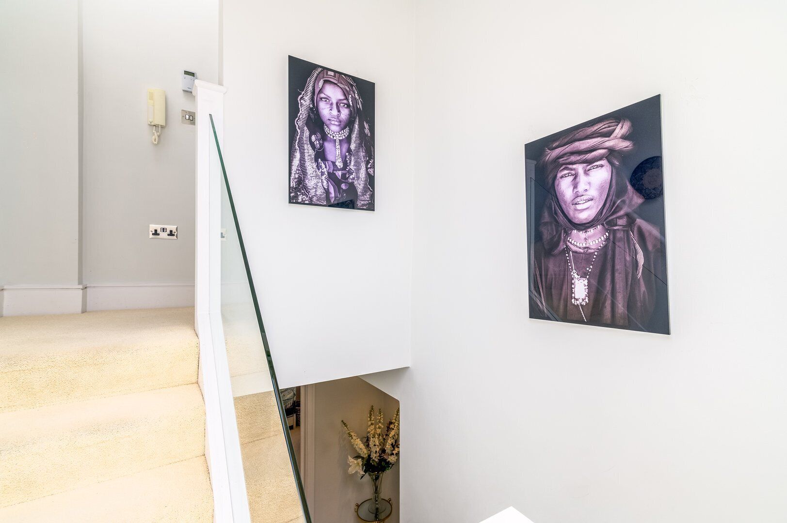 A hallway with a staircase, a phone, and two framed artworks on the wall.