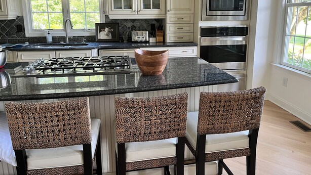 A kitchen with white cabinets, a gas stove, a microwave, and a large island with chairs. - Comfortable, bright home with heated pool/spa, large deck, and yard.   (Cape May)