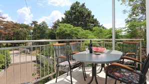Ein Balkon mit rundem Tisch, Stühlen, einer Flasche und einer Wassermelone.