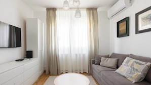 A modern living room with a grey sofa, a round coffee table, a TV mounted on a white cabinet, and a large window with sheer curtains. - La Porte - cozy and modern apartment located in the heart of the capital. (Beograd)