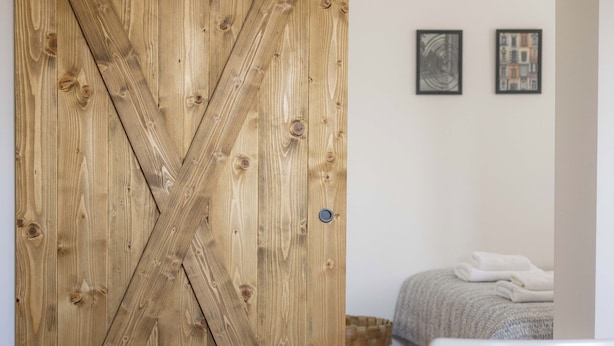 A room with a wooden sliding barn door, a bed with a white blanket, a white table, and a white chair. - La Porte - cozy and modern apartment located in the heart of the capital. (Beograd)