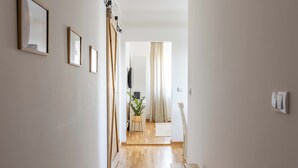 A hallway with wooden flooring, framed pictures on the wall, a plant, and a television in the background. - La Porte - cozy and modern apartment located in the heart of the capital. (Beograd)