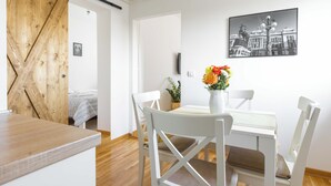 A dining area with a white table, white chairs, and a vase of flowers. There is a wooden door and a framed picture on the wall. - La Porte - cozy and modern apartment located in the heart of the capital. (Beograd)