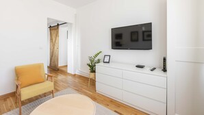 A modern living room with a flat-screen TV mounted on the wall, a white console table, a yellow armchair, and a wooden floor. - La Porte - cozy and modern apartment located in the heart of the capital. (Beograd)