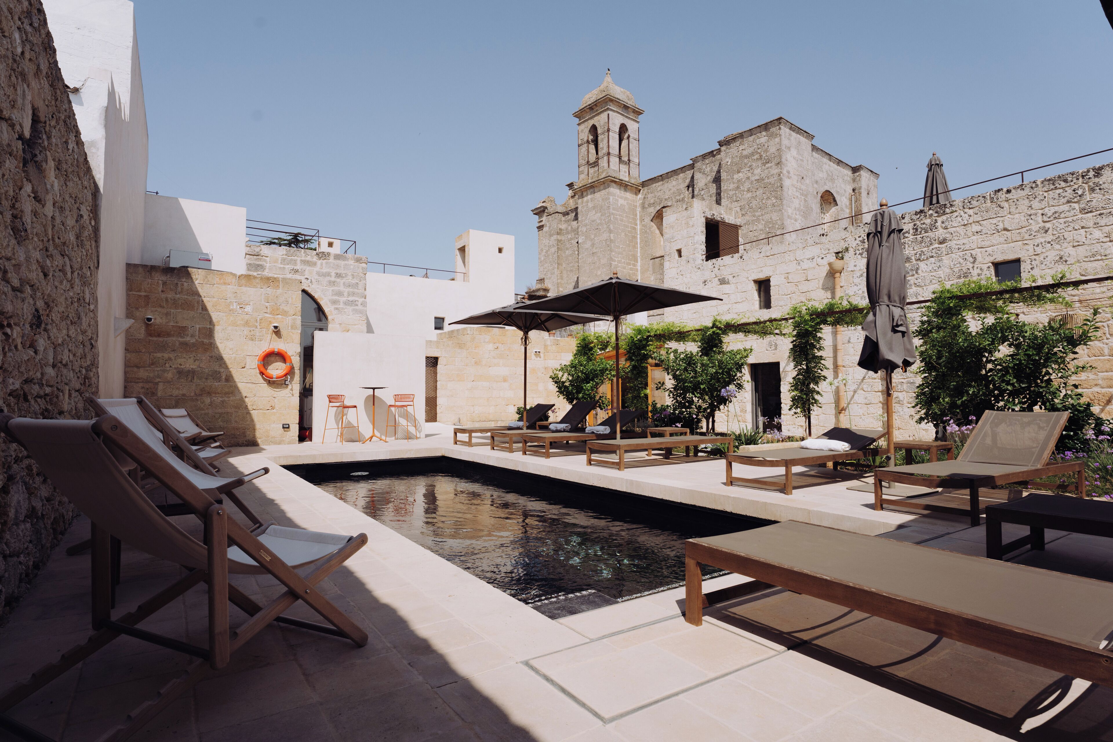 A courtyard with a swimming pool, lounge chairs, and a historic building with a bell tower.