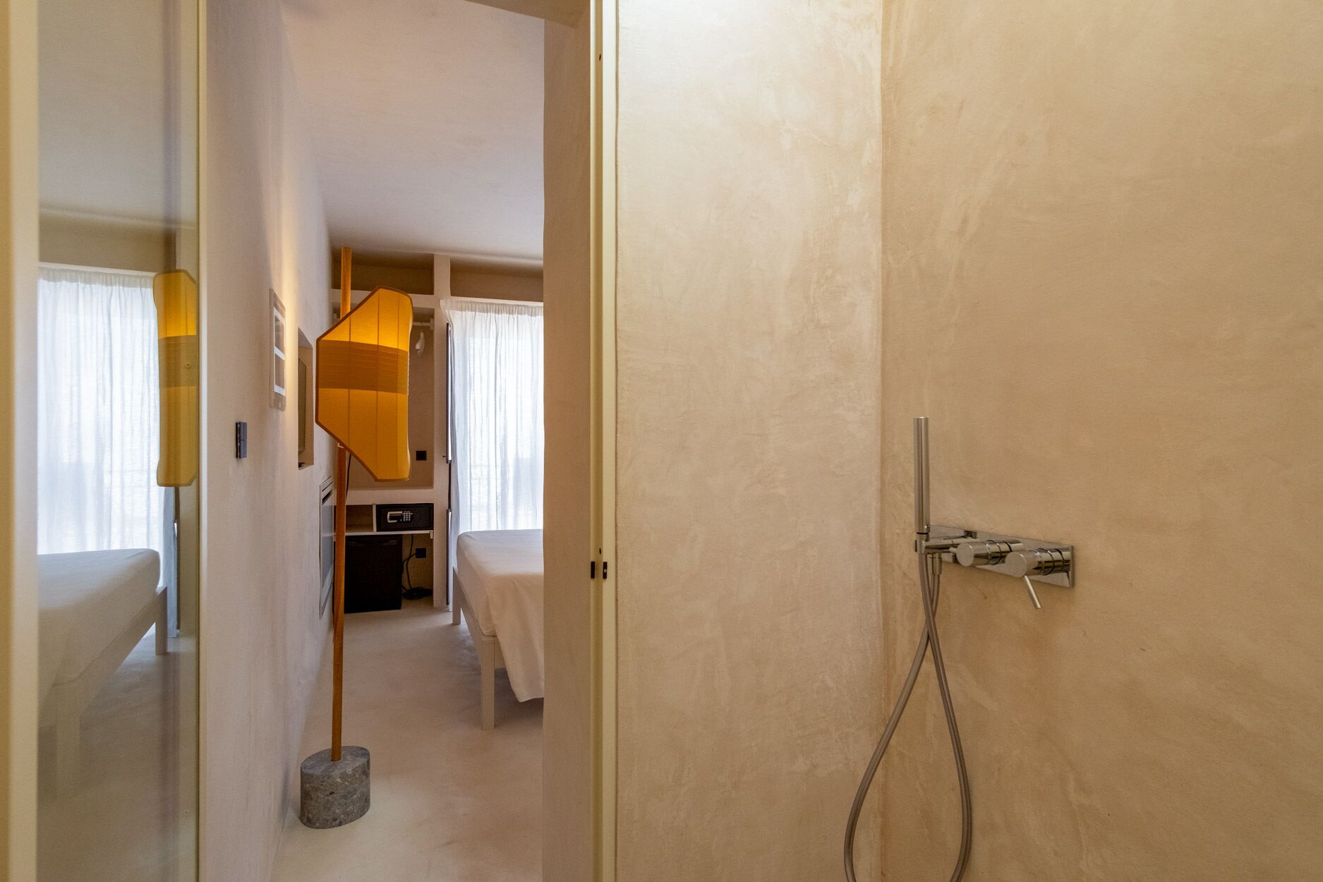 A hotel room with a bed, a desk, a lamp, and a shower area.