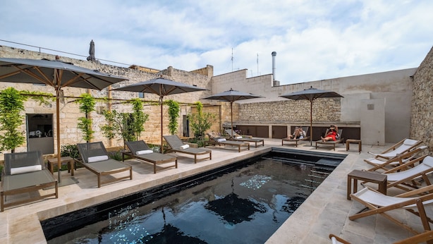 A rooftop pool area with lounge chairs and umbrellas, surrounded by stone walls and greenery. - I Tre Bacili (Spongano)