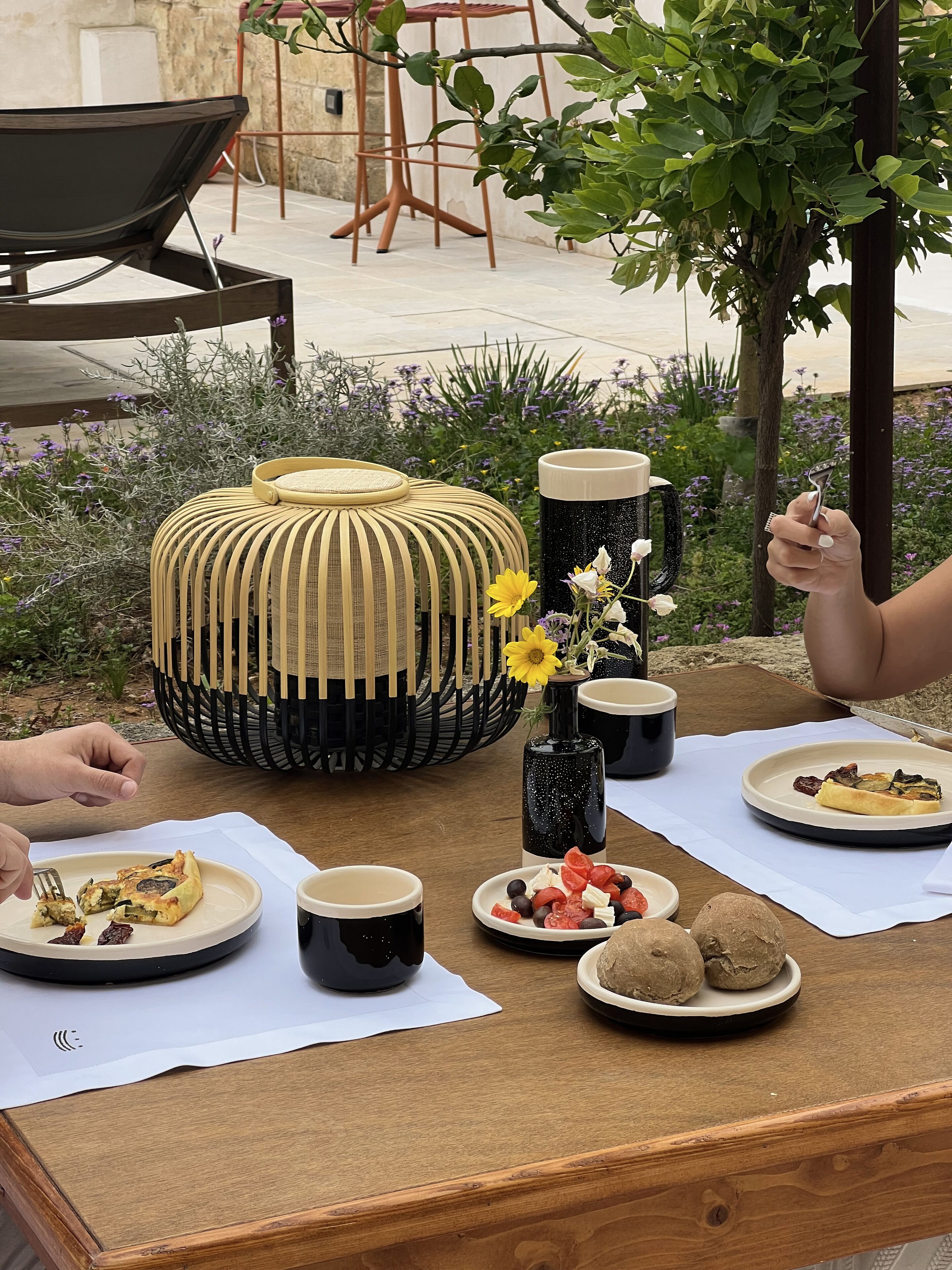 A dining table with plates of food, cups, and a decorative vase with flowers.