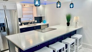 Una cocina moderna con una isla central, taburetes de bar, un refrigerador e iluminación colgante.