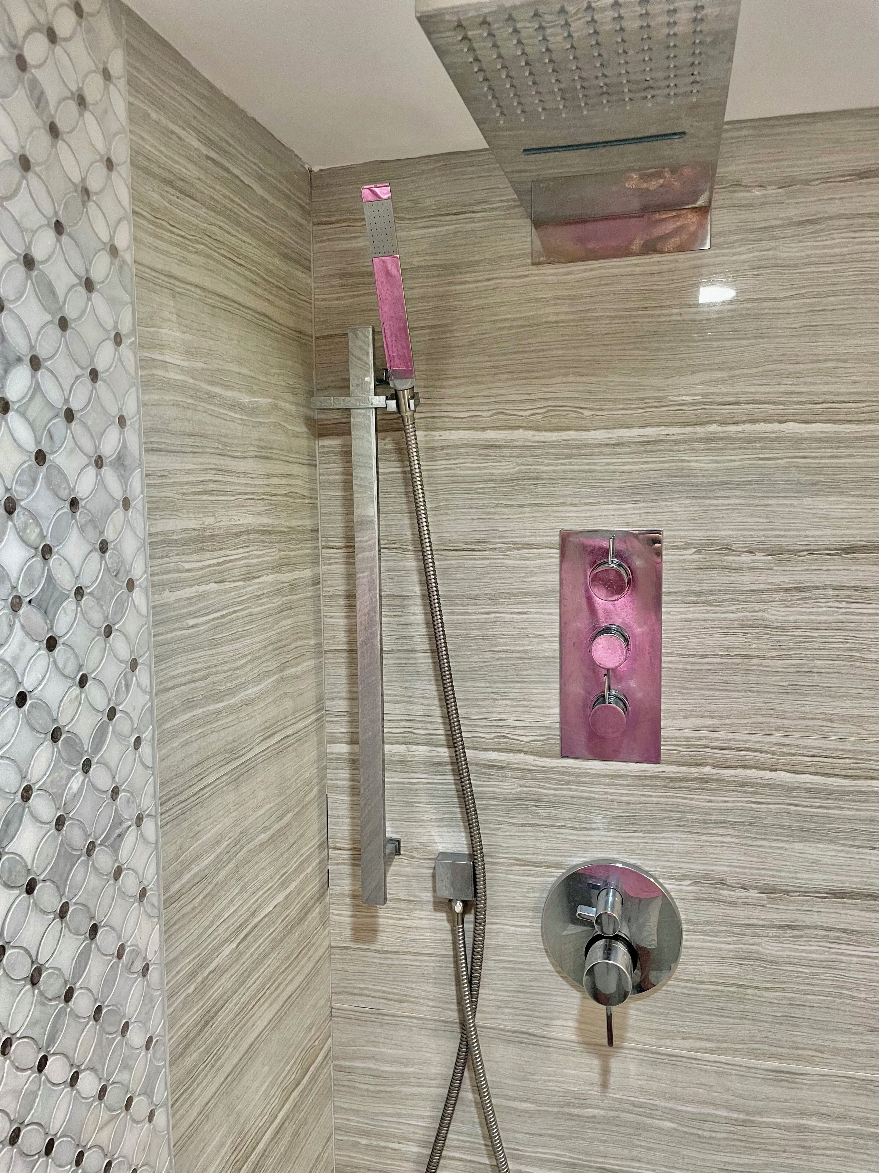 Une douche équipée d’un pommeau de douche à main et d’un panneau de commande fixé au mur.