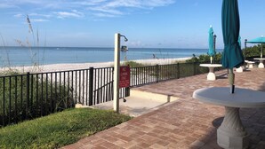 Un patio frente a la playa con un letrero que dice 'NO CLIMBING FENCE', vista al océano y algunas personas en la playa.