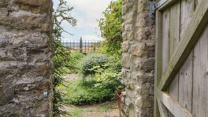 A narrow stone pathway leading to a wooden door, surrounded by lush greenery and a stone wall. - Hepple Hill Cottage (Consett)