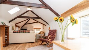 A cozy attic bedroom with exposed wooden beams, a wooden dresser, a rocking chair, and a vase with sunflowers. - Hepple Hill Cottage (Consett)